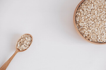 Dry oatmeal in a wooden plate and spoon on a white background. Top view. Copy, empty space for text