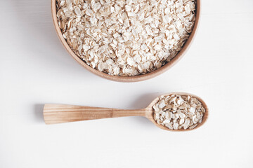 Dry oatmeal in a wooden plate and spoon on a white background. Top view. Copy, empty space for text