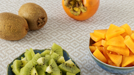 Persimmon and kiwifruit pieces in small bowls. Copped row fruits snack salad.