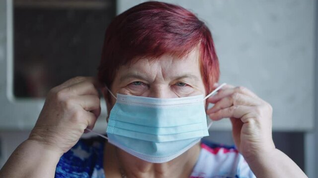 Senior woman putting on medical mask and looking at camera. Closeup aged person staying at home and social distancing during lockdown. Concept of healthcare