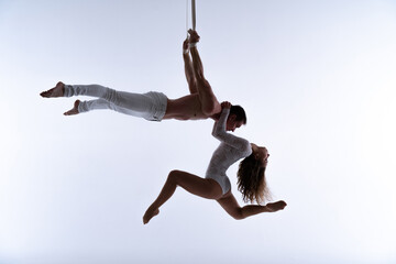 Aerial straps duo wearing white costume on white background doing performance 