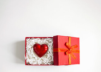 Red heart between crinkle cut paper in gift box on white background. Valentine day card with copy space, top view.