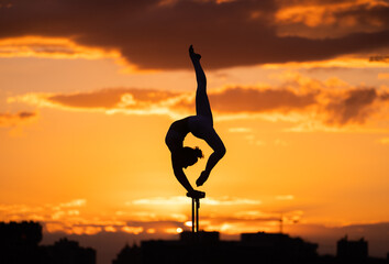 Flexible female circus Artist keep balance and doing contortion on the rooftop against dramatic...