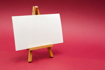 Wooden easel with white sheet. Red background.