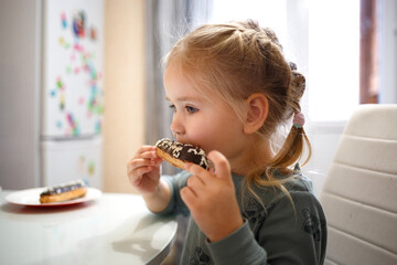 little cute girl eating cake while sitting at the kitchen table