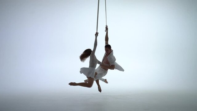 Aerial straps duo wearing white costume on white background doing performance 