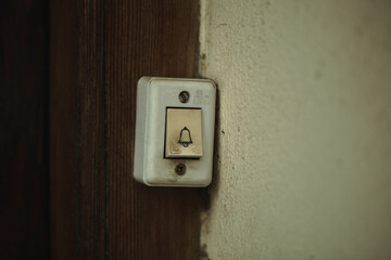 Close up on a filthy old electric doorbell fitting on a wooden door with bell icon on the button. This is a lighter version, a darker version is also available in the portfolio