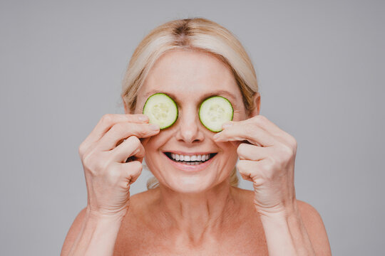 Cheerful Healthy Mature Woman Holding Cucumber Slices On Eyes Isolated Over Grey Background