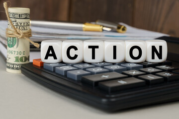 There are cubes on the calculator that say - ACTION. Nearby out of focus - dollars, notebook and pen