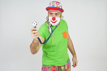 The clown plays doctor, bugs himself with a stethoscope. Isolated on white