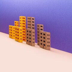 The concept of distortion and change of urban space. Distorted and tilted miniature city. Yellow brown houses on purple beige background. Abstract urban architecture landscape, simplified town layout.