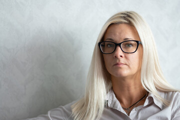 A strict young blonde woman with glasses looks at the camera. Optical