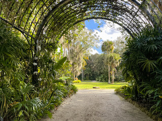A pathrway surrounded by an arch trellis that opens into a botanical garden