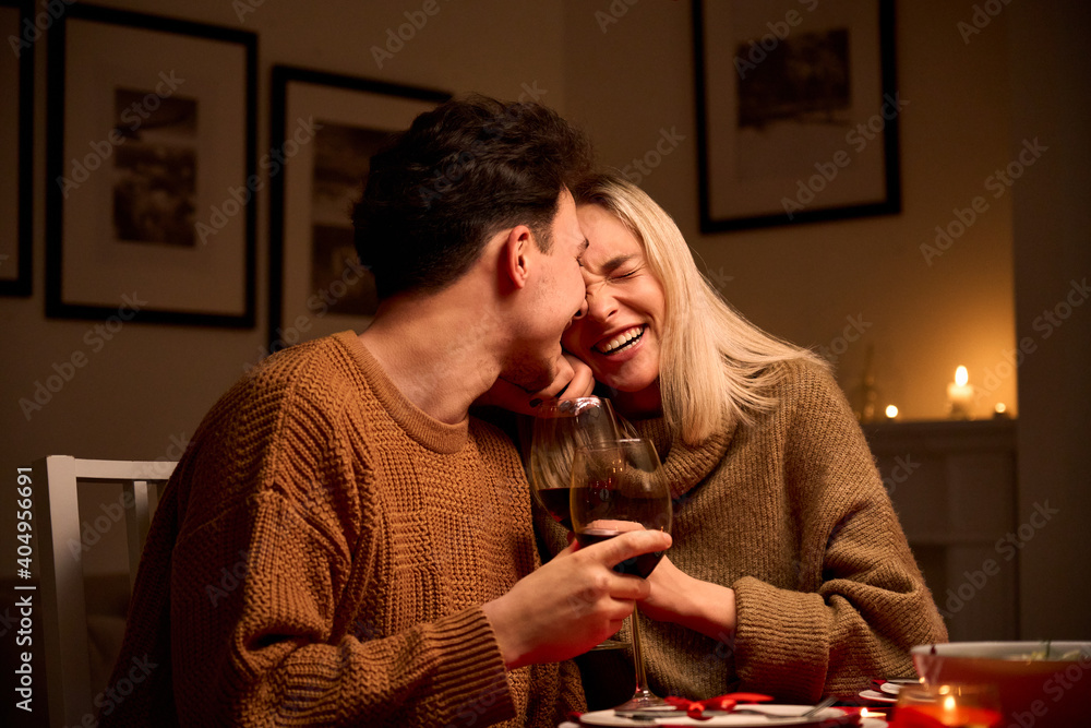 Wall mural happy young couple in love hugging, laughing, drinking wine, enjoying talking, having fun together c