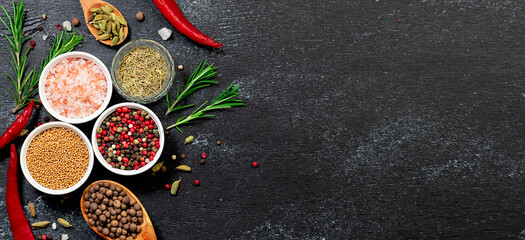 Assortment of aromatic organic spices and herbs on black rustic background long banner format. Healthy tasty food concept.