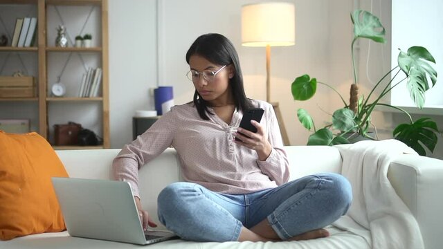 African woman working background home interior distant from office Spbd. Black female model with computer on couch and phone in hand is running an assignment from online management. At house employee