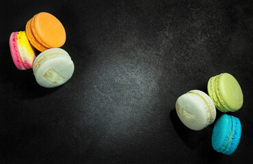 Multi-colored bright macarons are laid out on a black background.