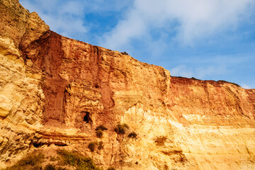 Fototapeta premium rocks on the shore of benagil beach in portugal. sandy orange embankment hill against blue sky.