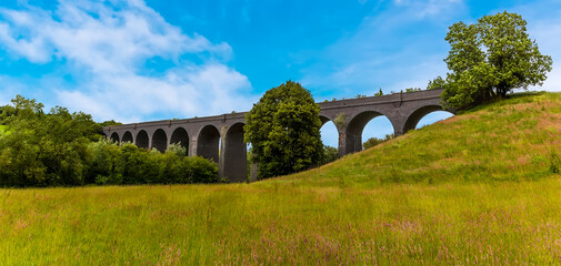 A panorama view across a grassy meadow of the derelict and abandoned viaduct near Catesby, Northamptonshire, UK