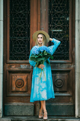 Fototapeta na wymiar Summer portrait of a beautiful woman with flowers of hydragea in front of vintage doors