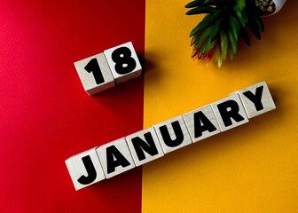 January 18 in black letters on wooden blocks on a divided yellow-red background .Next to a flower...