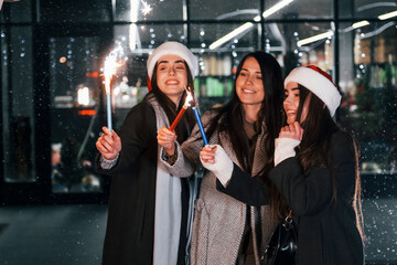 Little fireworks, Bengal lights. Three cheerful women spends Christmas holidays together outdoors. Conception of new year