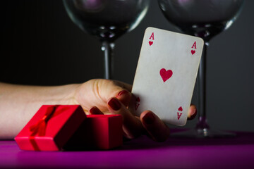 Valentines day creative concept. Gift box and a hearts playing card with wine glasses in the background. 