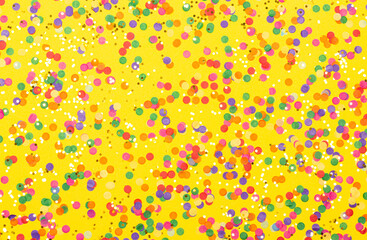 Scattered confetti on yellow background. Holiday decoration concept. Restive backdrop for your design.