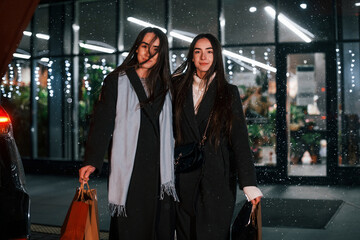 Obraz premium Walks with packages. Just from shopping. Happy sisters twins spends Christmas holidays together outdoors. Conception of new year