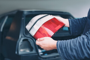 A mechanic installs taillights in a new car at a car service. A man holds a headlight in his hands.