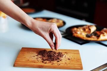 The hand of pastry chef with grated chocolate. Going to sprinkle the cake