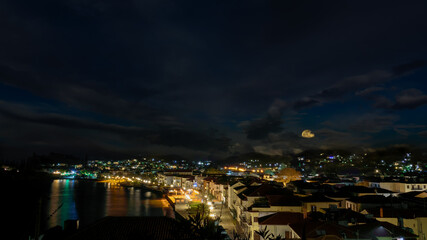 Fototapeta na wymiar The city of Myrina in Greece, under the cloudy night sky with the full moon