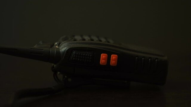 The black radio is on the table. Police device. Safety system. Line for negotiations. Remote receiver-transmitter. Flashing signal lights. blue and red light. Dark background. Night. Close-up view.