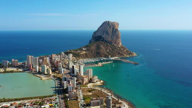 Penyal d'Ifac Natural Park near Calp city, Spain. Beautiful rock near buildings of the city close to the beach full of tourists - aerial view with a drone 4K