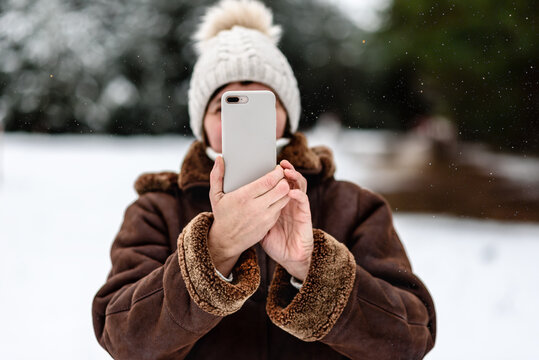 Woman takes a picture on mobile phone in the forest on a cold winter day.