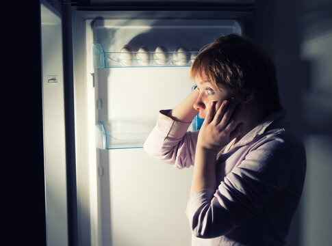 Side View Of Shocked Woman Looking In Empty Refrigerator At Home