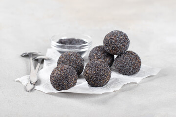 Raw candy balls made of dates, sunflower paste, with poppy seeds on paper on a light gray background