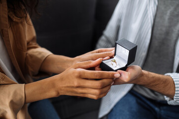 Close-up photo of an caucasian man gives an engagement ring to his beloved african american woman, she gladly accepts it