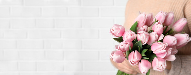 Woman with beautiful pink spring tulips near white brick wall, space for text. Horizontal banner...