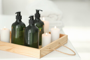 Wooden tray with soap dispensers and burning candles on white table. Space for text