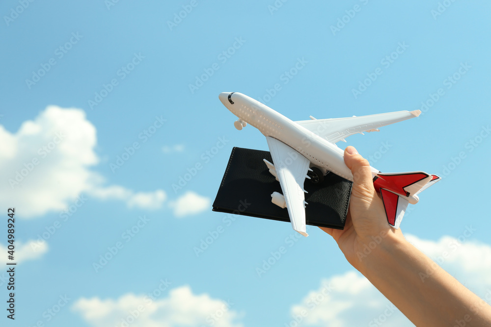 Poster Woman holding toy airplane and passport against blue sky, closeup