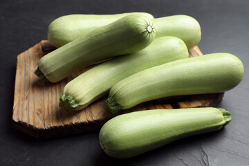 Raw green zucchinis and wooden board on black slate table