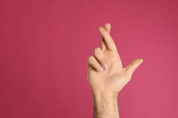 Naklejka premium Man with crossed fingers and space for text on pink background, closeup. Superstition concept