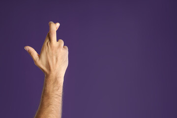 Man with crossed fingers and space for text on purple background, closeup. Superstition concept