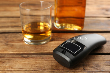 Modern breathalyzer and alcohol on wooden table