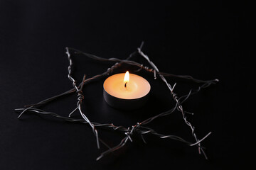 Burning candle and star of David made with barbed wire on black background. Holocaust memory day