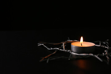Burning candle and star of David made with barbed wire on black background, space for text....
