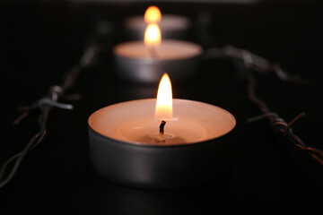 Burning candle and barbed wire on black background, closeup. Holocaust memory day