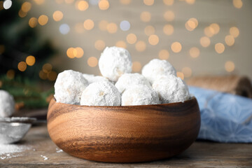 Fototapeta na wymiar Tasty snowball cookies in wooden bowl against blurred festive lights. Christmas treat