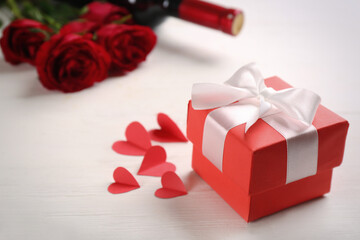 Beautiful gift box and paper hearts on white wooden table, space for text. Valentine's Day celebration